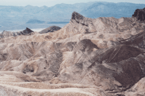 A barren, eroded desert landscape with layered sedimentary rock formations under a hazy sky.