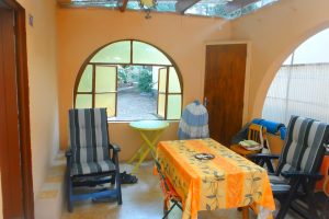 A bright and inviting patio area featuring striped chairs, a yellow tablecloth, and a large window that opens to a green outdoor space.