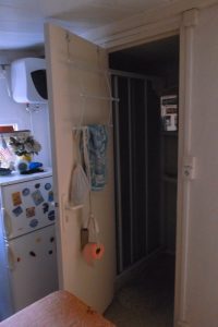 View of an open door leading to a hallway, with kitchen appliances and a decorated wall visible in the background.