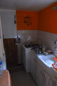 A small kitchen featuring an orange accent wall, equipped with a sink, stove, and various cooking utensils.