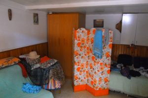 A cozy interior featuring a floral screen, furniture with colorful textiles, and scattered clothing items.