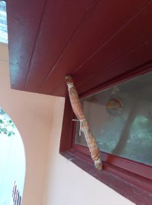 A close-up of a curtain rod wrapped in fabric, attached to a red wooden edge near a window.